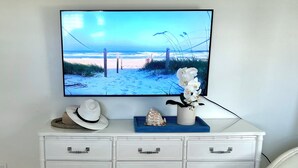 A white dresser with drawers and a flat-screen TV displaying a beach scene.