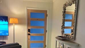 A living room with a green carpet, a sofa, a TV, a lamp, a door with blue panels, and a shelf with decorative items.
