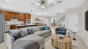 A modern living room with a sectional sofa, a round coffee table, and a dining area with wooden cabinets and a kitchen in the background. - Daisy Townhouse Villas Step from the beach (pompano beach)