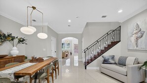 A spacious living area with a wooden dining table, a sofa, and a staircase with a decorative railing. - Daisy Townhouse Villas Step from the beach (pompano beach)