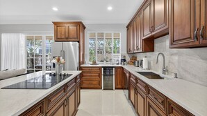 A modern kitchen with wooden cabinets, a stainless steel refrigerator, and a large island with a built-in stove. - Daisy Townhouse Villas Step from the beach (pompano beach)