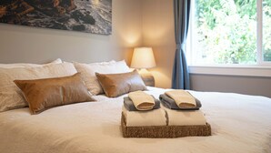 A neatly made bed with a lamp, pillows, and a basket of folded towels.