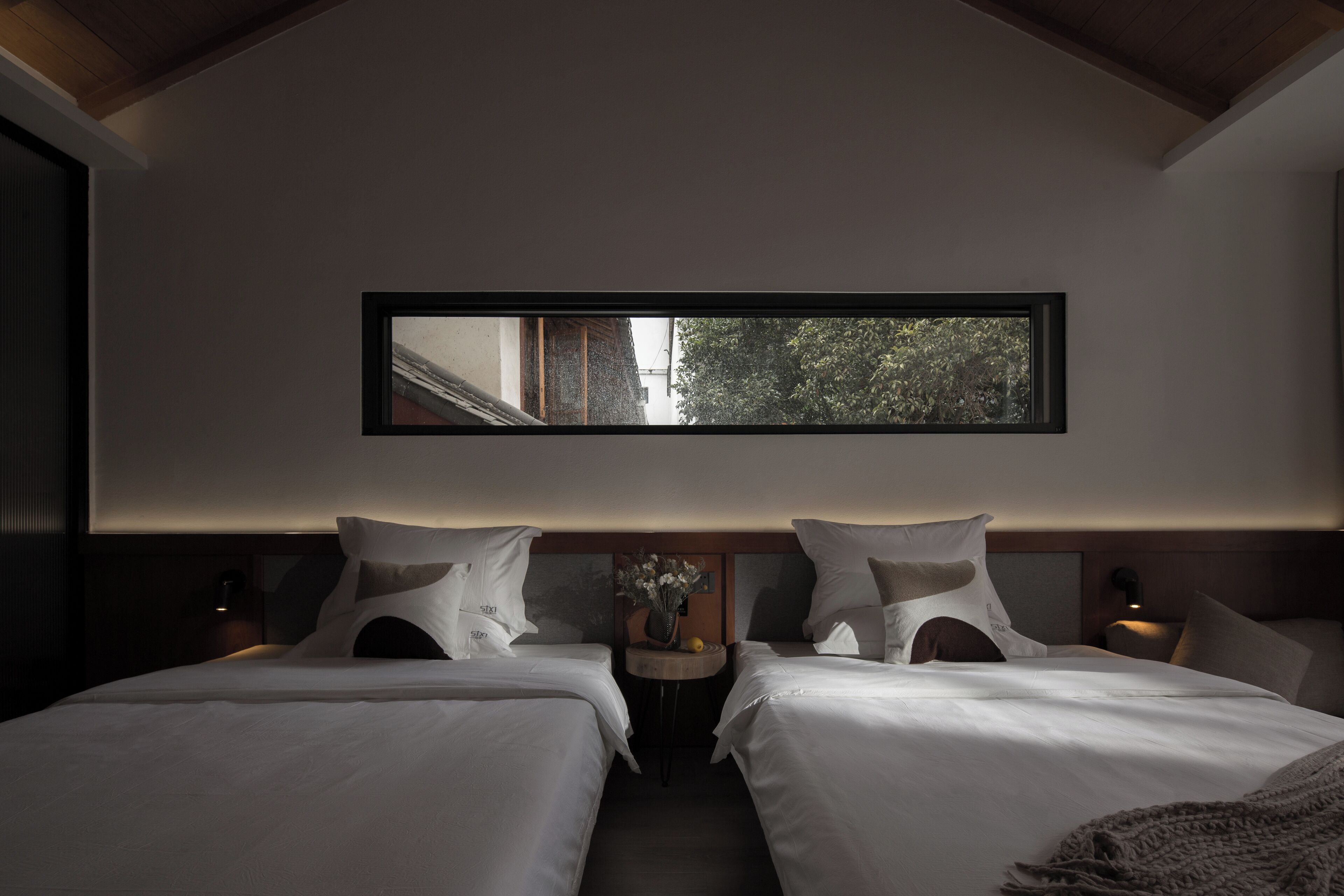 Una habitación de hotel moderna con dos camas, un ventanal amplio y una pequeña mesa con un florero.
