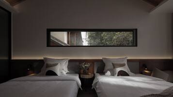 Una habitación de hotel moderna con dos camas, un ventanal amplio y una pequeña mesa con un florero.