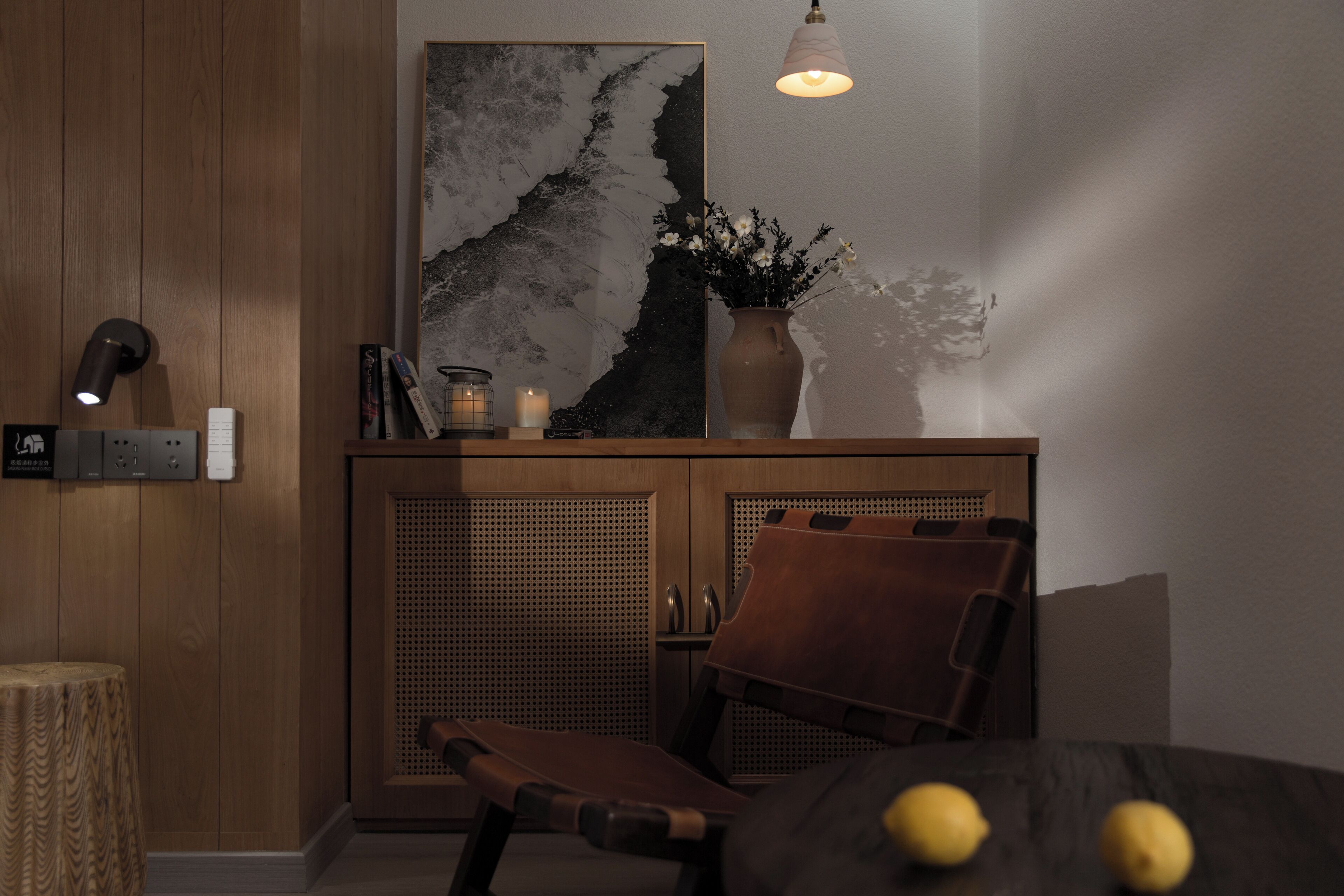 A modern room with a wooden cabinet, a chair, a vase with flowers, and a wall-mounted light fixture.