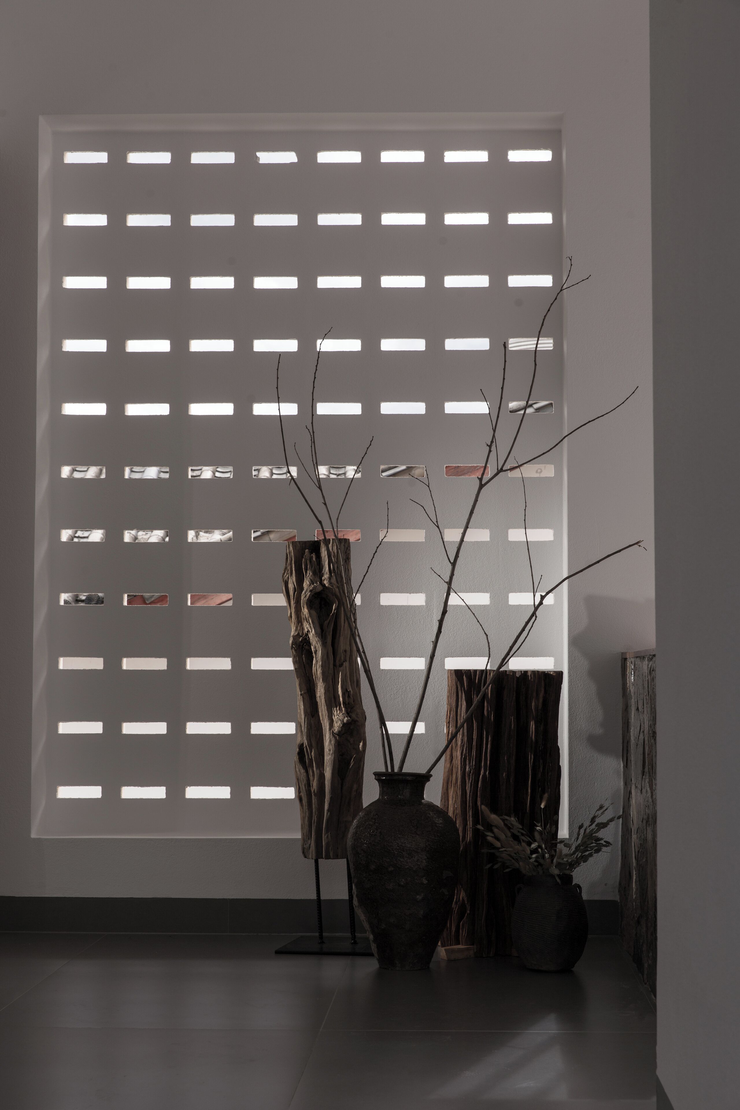 A room with a large window featuring a grid pattern, a rustic wooden sculpture, and two vases with plants.