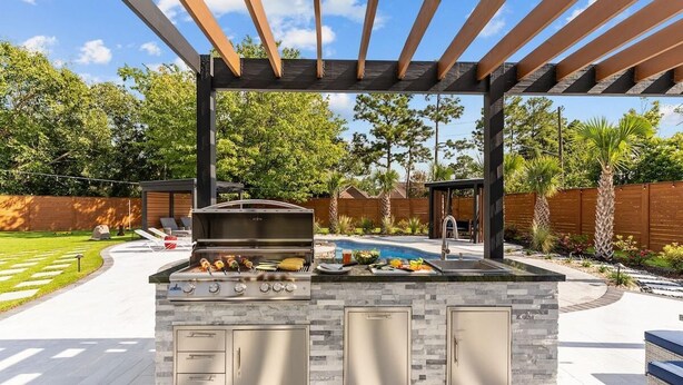 Een buitenkeuken met een barbecue, twee spoelbakken en een pergola erboven.
