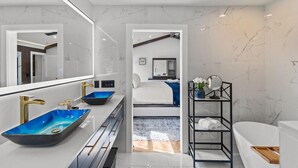 Een moderne badkamer met een grote spiegel, een blauwe wastafel, een zwart plankje en een witte badkuip.