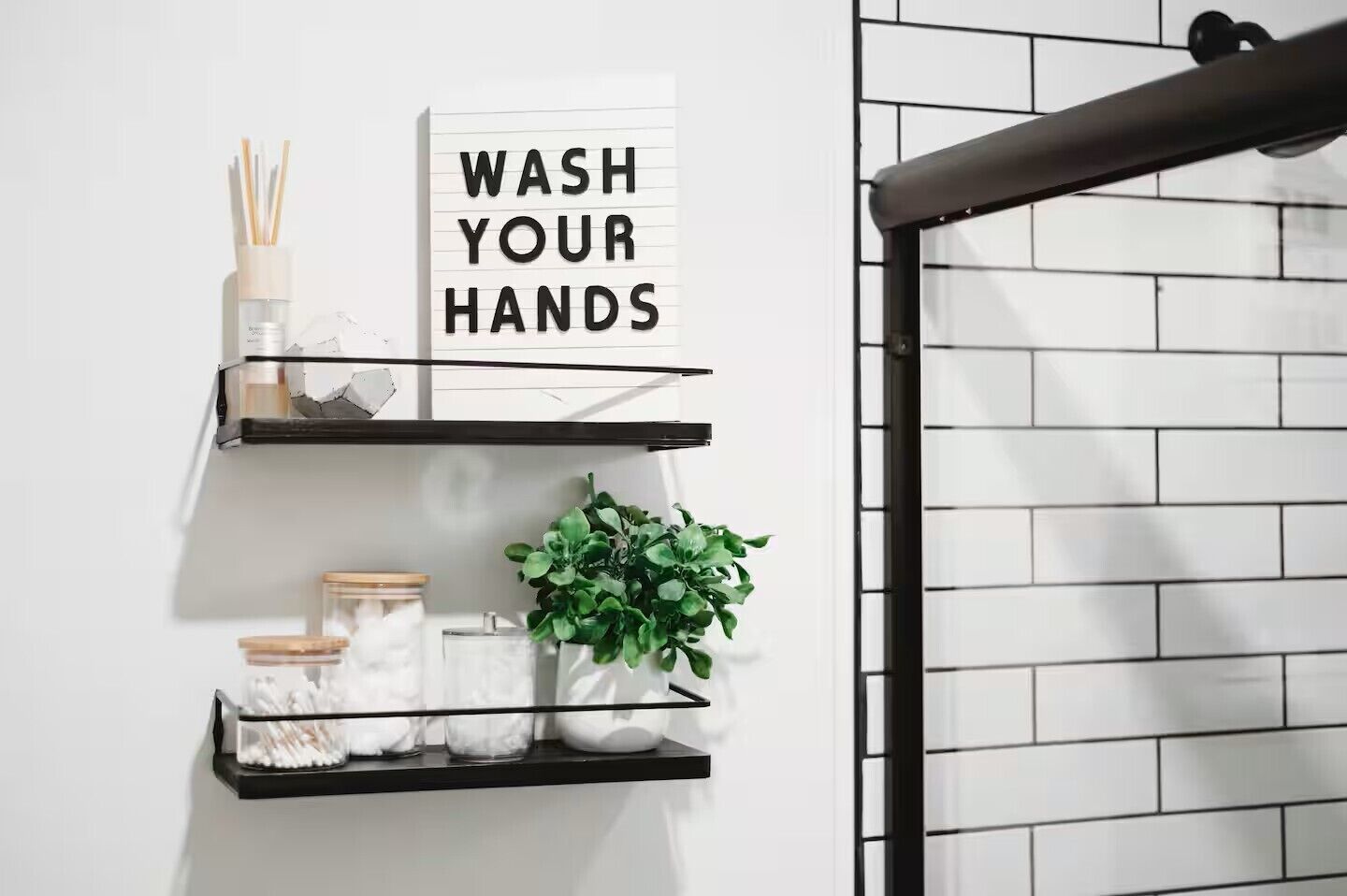 Une salle de bain avec un panneau indiquant qu’il faut se laver les mains, une étagère avec une plante et un porte-serviettes.