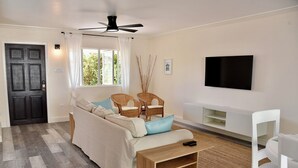 Ein Wohnzimmer mit einer Couch, zwei Korbstühlen, einem Holztisch, einem Flachbildfernseher und einem Deckenventilator.