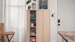 Une cuisine avec un meuble en bois, une chaise en osier et une porte avec une boîte aux lettres.