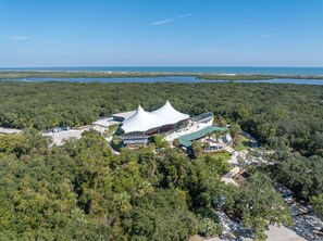 An aerial view of a resort with a distinctive white tent-like structure surrounded by dense forest and a body of water in the background. - Madeira Suite: Steps to Music, Markets & Florida Sun (St. Augustine)