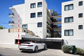 A modern multi-story building with a white facade, multiple balconies, and a gated entrance with a white car parked in front. - Luxury Cabo Studio | Rooftop Pool, Hot Tub & Walk to Beach (Cabo San Lucas)