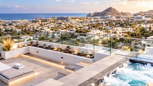 A rooftop terrace with a pool, seating areas, and a view of the city and mountains. - Luxury Cabo Studio | Rooftop Pool, Hot Tub & Walk to Beach (Cabo San Lucas)