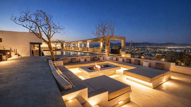 A modern outdoor lounge area with a fire pit and seating, overlooking a cityscape at dusk. - Luxury Combo Suite | Rooftop Pool & Walk to Beach (Cabo San Lucas)