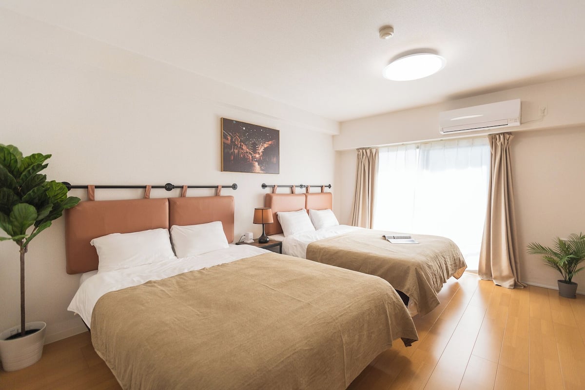 A hotel room with two beds, a nightstand, a lamp, an air conditioner, and a window with curtains.