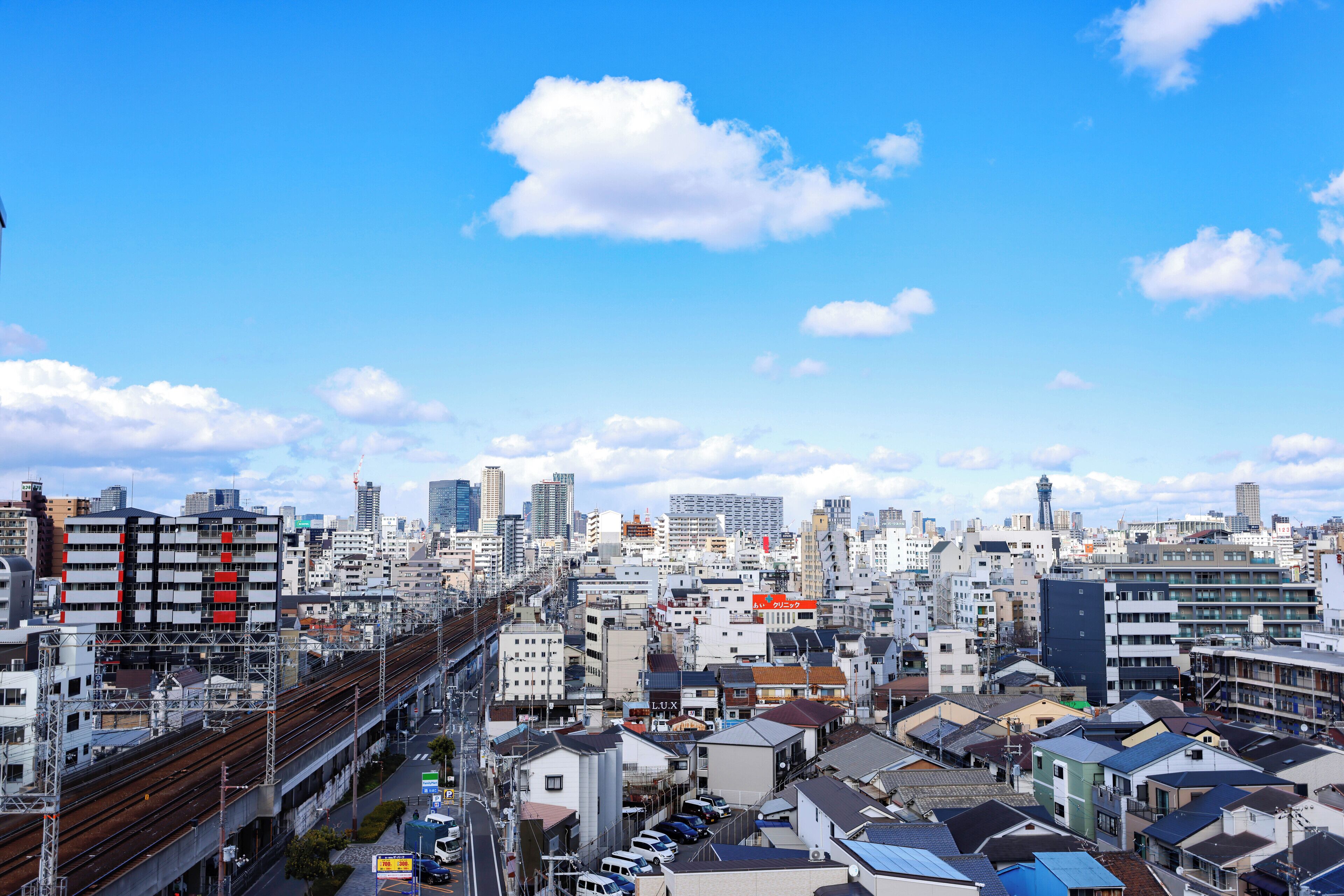 Un paisaje urbano con edificios residenciales densos, una vía ferroviaria destacada y un cielo azul despejado.
