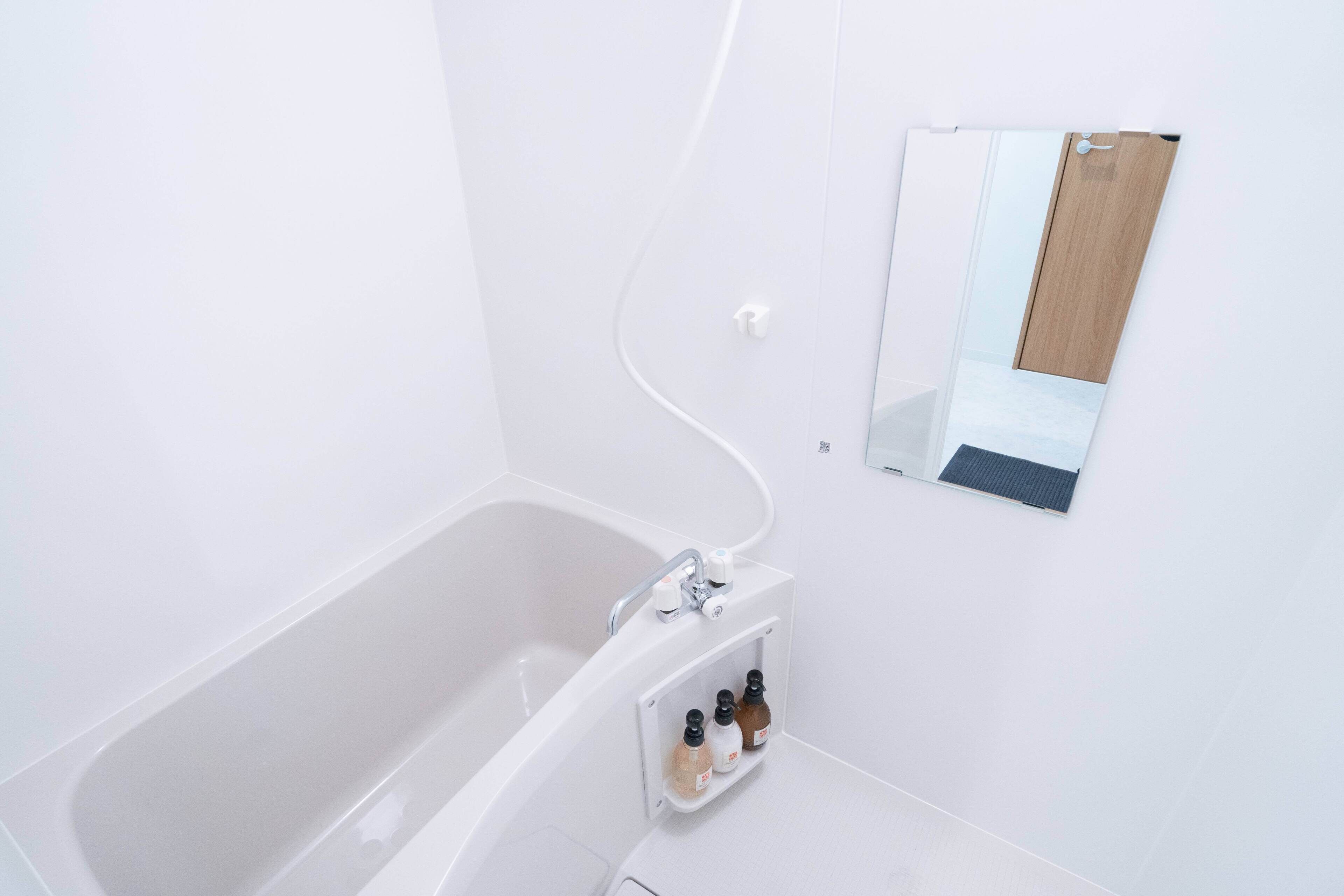 Un baño moderno con una bañera blanca, un espejo integrado y un dispensador de jabón.