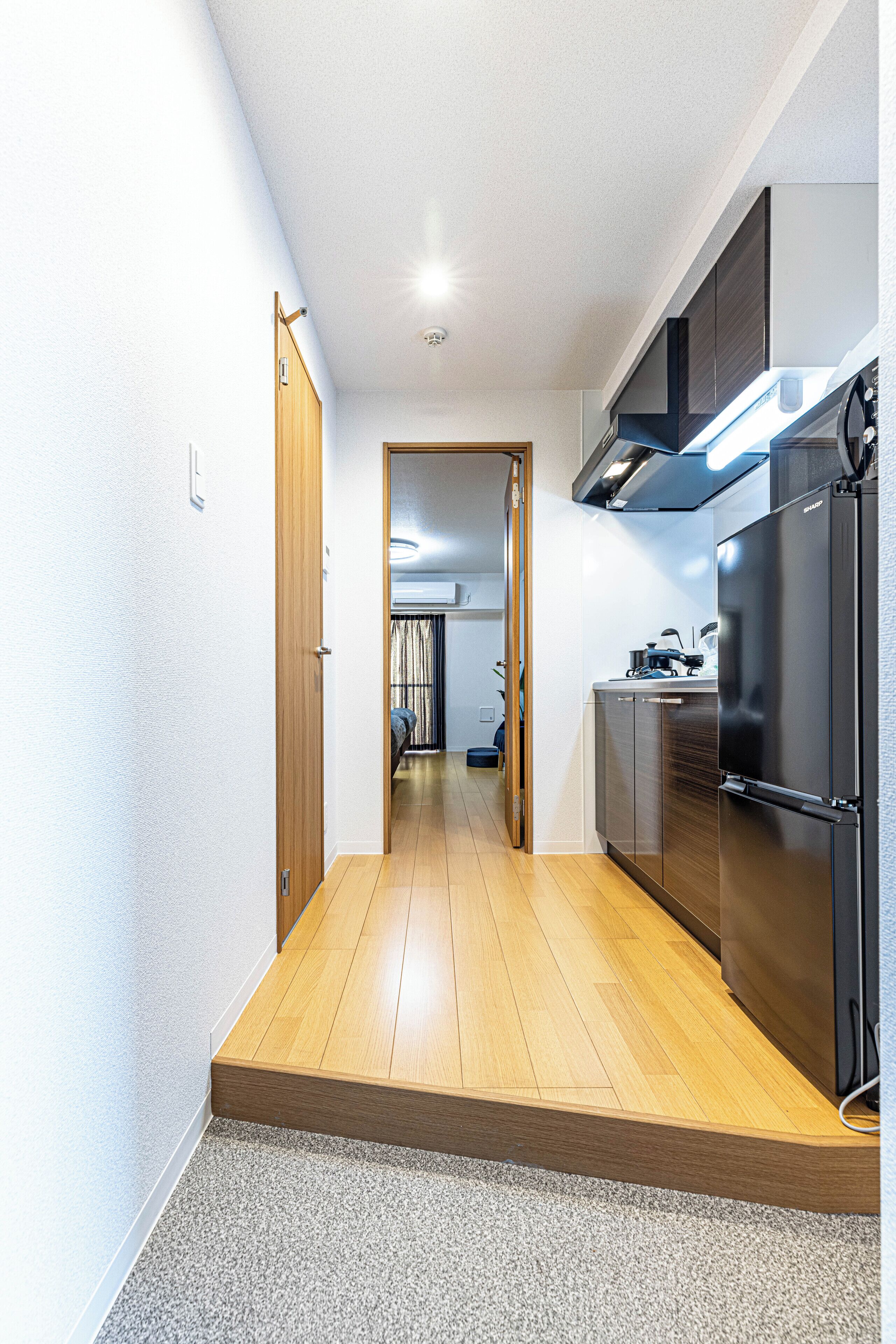 A narrow hallway with wooden flooring, a black refrigerator, and a door leading to another room.
