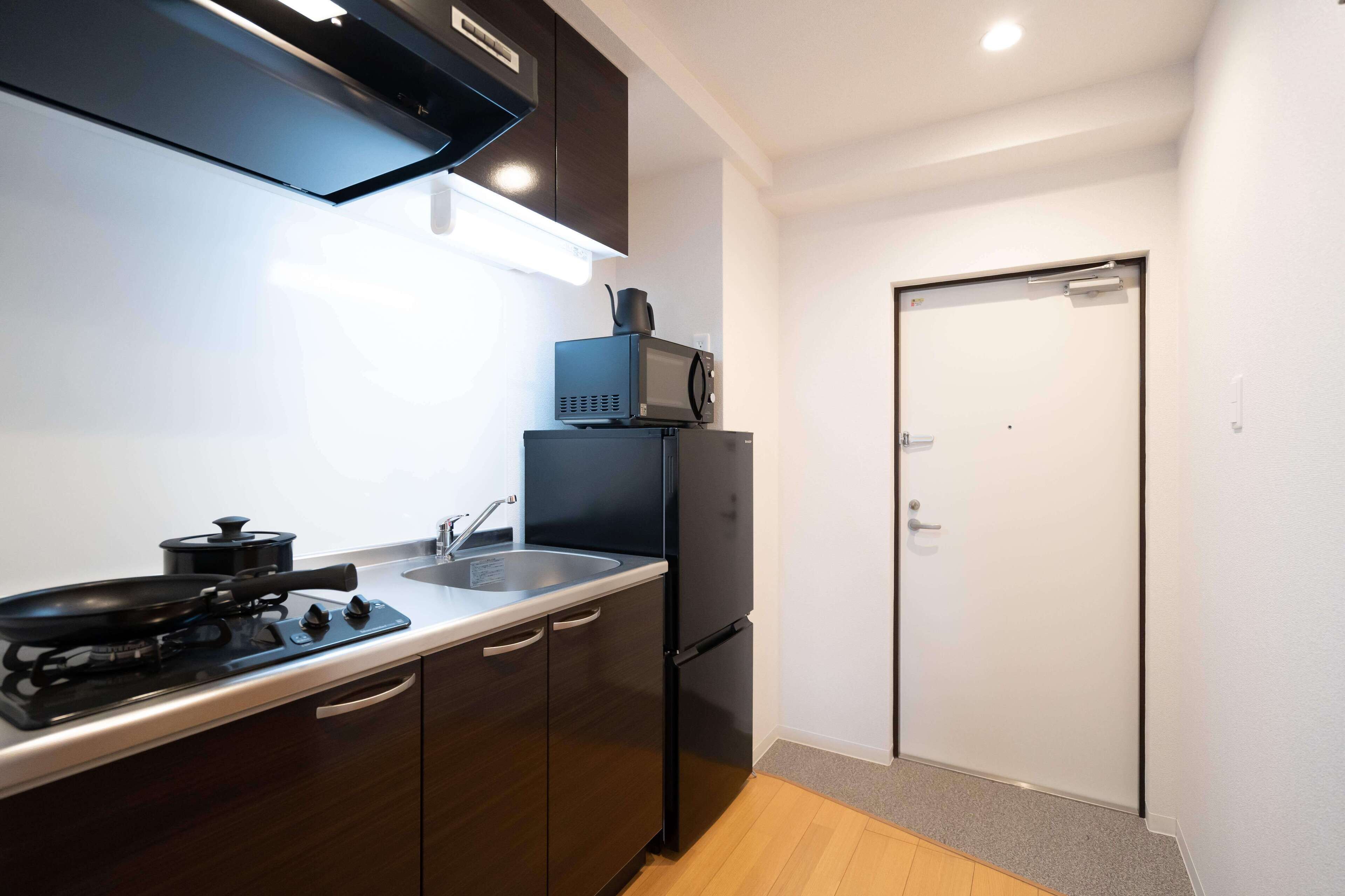 A compact kitchen with dark wooden cabinets, a black stove, a microwave, and a refrigerator.