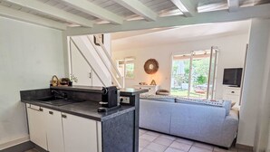 Een moderne keuken met een inbouw-kookeiland, een zithoek met een grijze bank en een groot raam met uitzicht op het landschap.