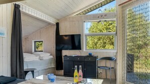 Une chambre confortable, aménagée dans le style d’un chalet, avec un lit, une télévision, une table à manger avec des chaises et une grande fenêtre donnant sur un paysage verdoyant.