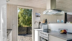 Une cuisine moderne dotée d’un four encastré, d’un four à micro-ondes et d’une grande fenêtre donnant sur une terrasse en bois.