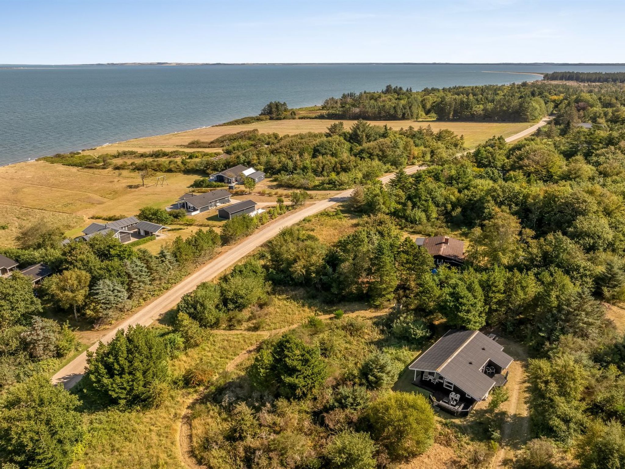Luchtbeeld van een woongebied met huizen, een onverharde weg en een waterpartij op de achtergrond.