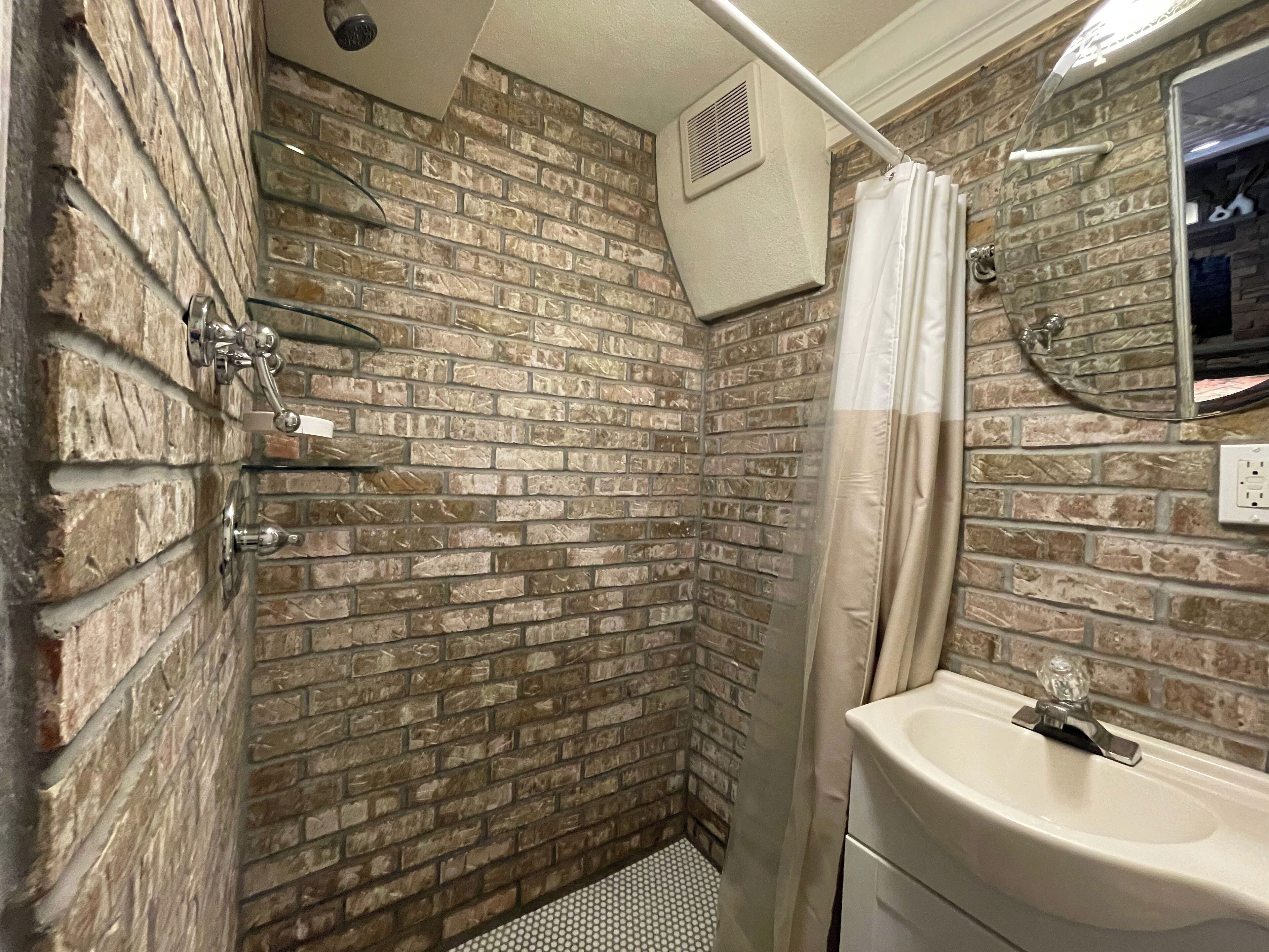 A bathroom with a brick wall, a shower curtain, a sink, and a mirror.