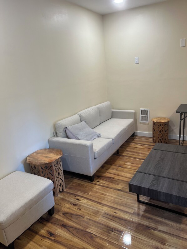 A living room with a grey sofa, a matching ottoman, a wooden coffee table, and a small side table.