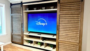 Un téléviseur à écran plat fixé sur un meuble de télévision en bois, doté d’étagères et accompagné d’une télécommande.