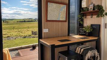 Una habitación con un escritorio de madera, dos taburetes negros, un mapa en la pared, un cartel de bienvenida y vistas a un campo verde.