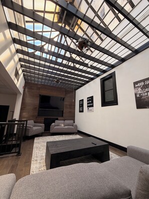 A modern living room with a high ceiling, large windows, and a flat-screen TV.