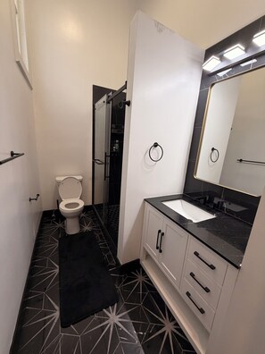 A bathroom with a toilet, sink, mirror, and shower.