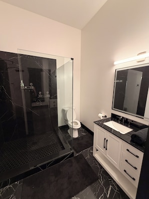 Ein modernes Badezimmer mit einer Duschkabine, einer Toilette, einem Waschbecken inklusive Spiegel und weißen Schränken.