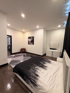 Ein modernes Schlafzimmer mit einem großen Bett, einem Flachbildfernseher, einer Kommode und einem Bild an der Wand.
