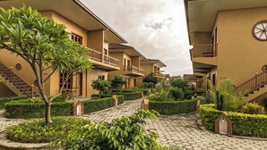 A hotel courtyard with a central pathway, surrounded by neatly trimmed hedges and small trees. - Munal and Mayur Resort (Kalika)