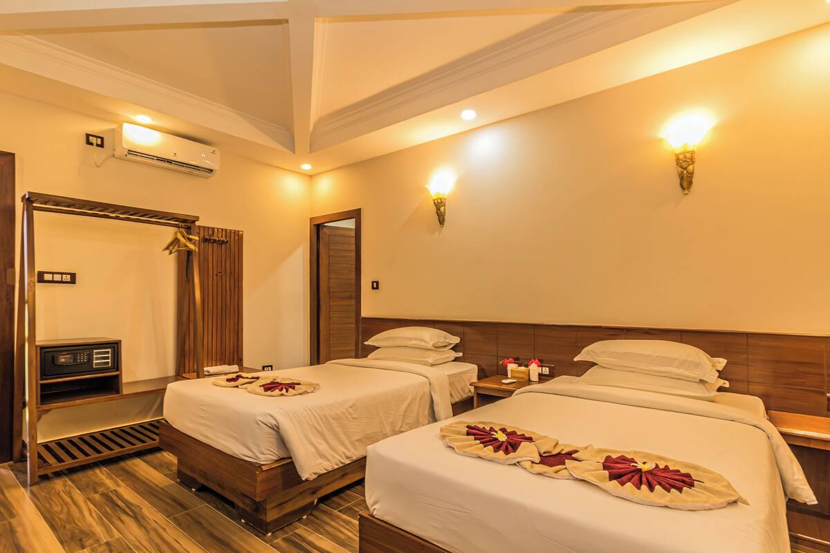 A hotel room with two beds, a wooden headboard, a bedside table with a lamp, an air conditioning unit, and a wardrobe with a mirror.