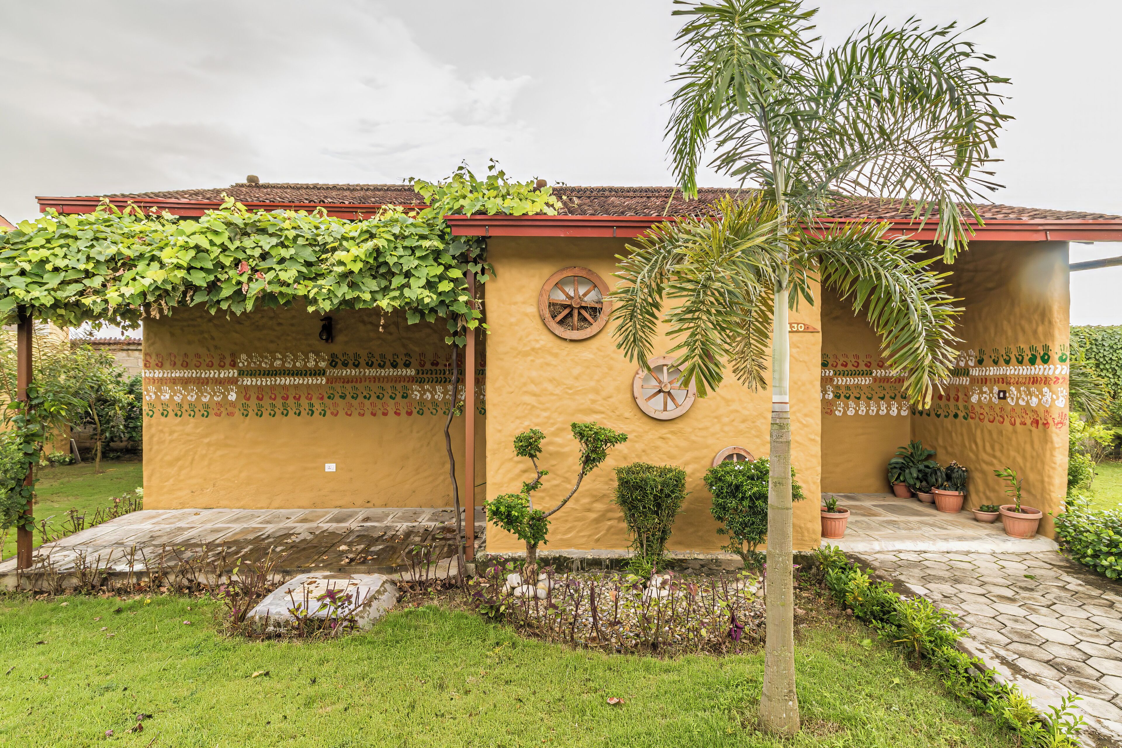 A building with a yellow exterior, a red roof, and a small garden area with potted plants and a palm tree.