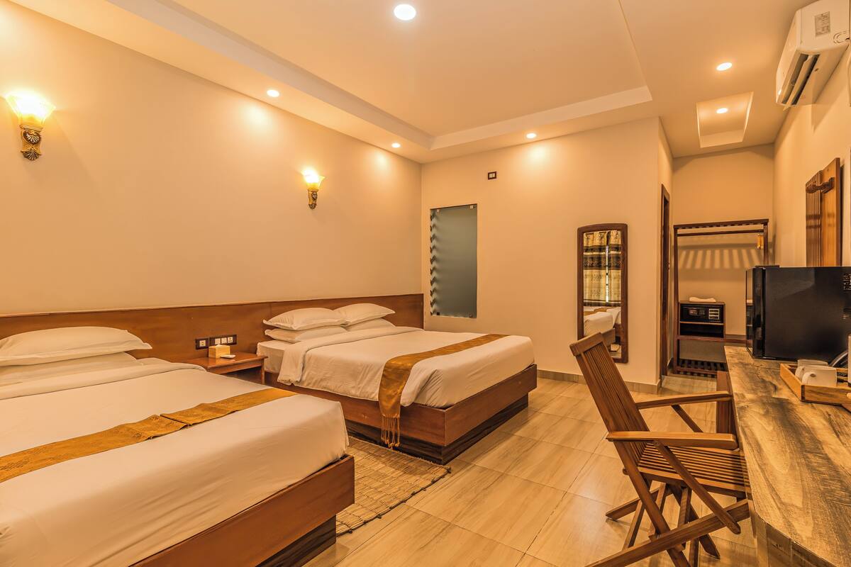 A hotel room with two beds, a desk, a chair, a TV, and a mirror.
