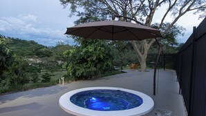 A hot tub with a surrounding patio area, a tree, and a fence.