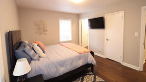 A bedroom with a bed, a lamp, a TV, and a patterned rug. - Cozy Decatur Bungalow with Beautiful Backyard (Decatur)