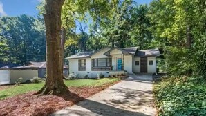 A single-story house with a front porch, a garage, and a yard with a tree and shrubs. - Cozy Decatur Bungalow with Beautiful Backyard (Decatur)