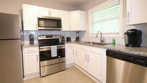 A modern kitchen with white cabinets, stainless steel appliances, and a granite countertop. - Cozy Decatur Bungalow with Beautiful Backyard (Decatur)