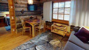 Interior acogedor de una cabaña de troncos con una mesa de comedor de madera, sillas, un sofá y un ventanal con cortinas.