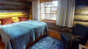 Una habitación tipo cabaña de madera con una cama, una silla y una ventana con cortinas.