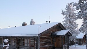 Una cabaña de troncos con techo nevado y porche de madera.