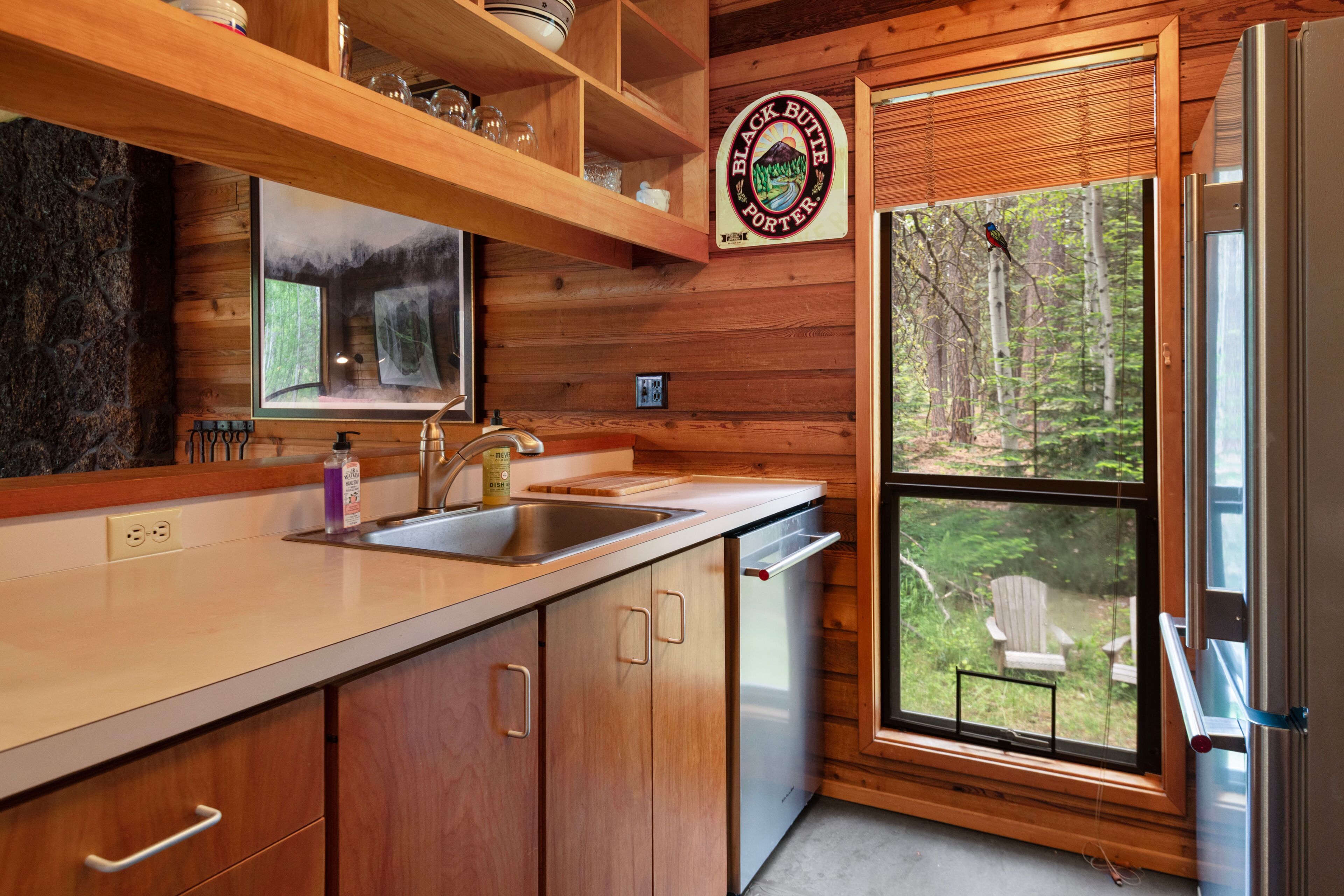 Une cuisine rustique aménagée dans une cabane en bois, avec une grande fenêtre, un évier et un réfrigérateur.