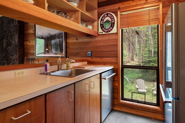 A wooden cabin kitchen with a large window, a sink, and a refrigerator.