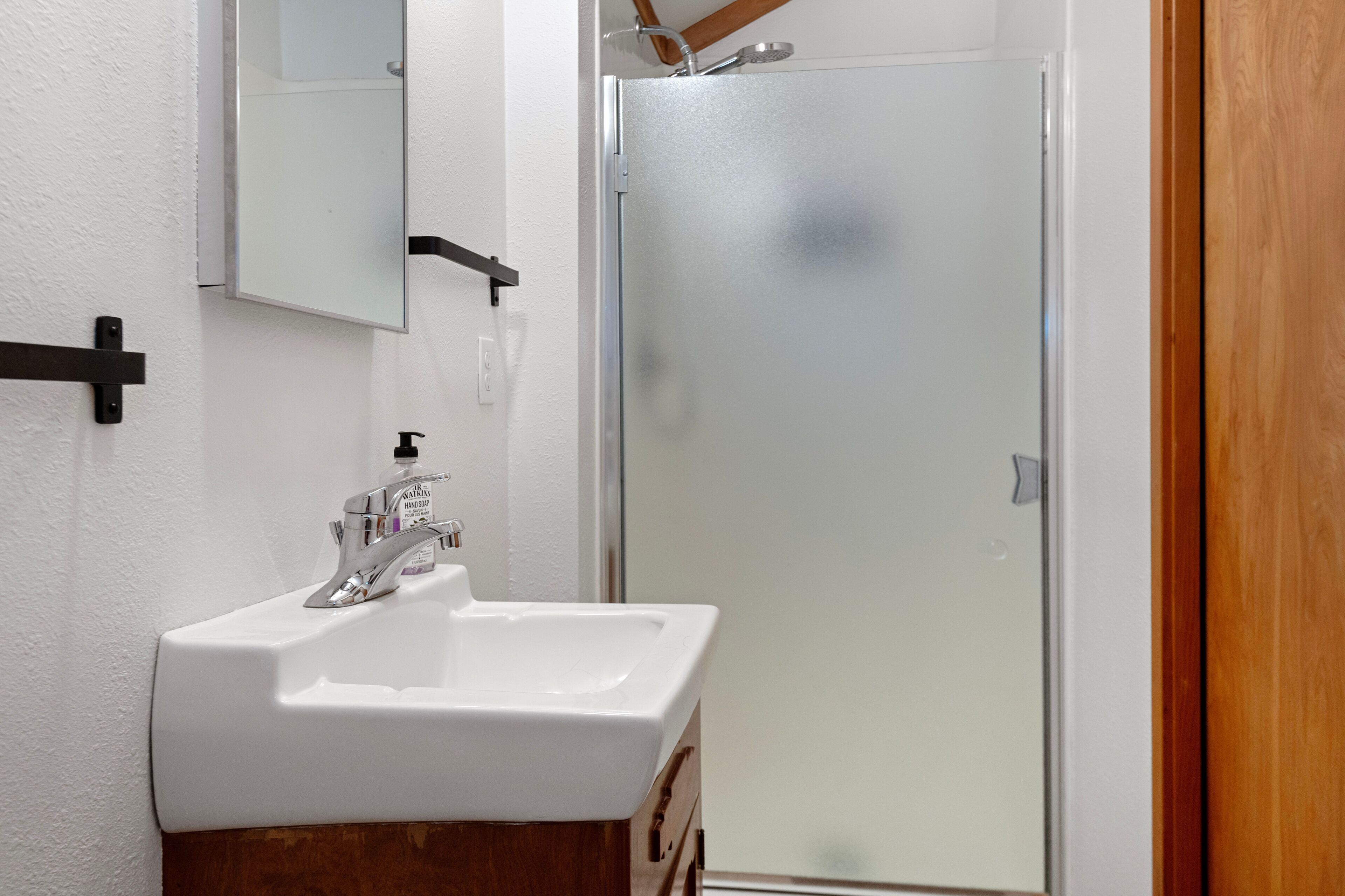 A bathroom with a white sink, a mirror, and a glass shower door.